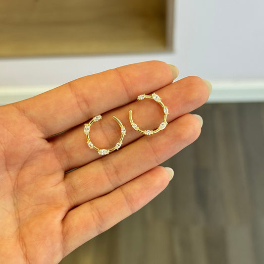 Gold hoop earrings held in a hand with a blurred background